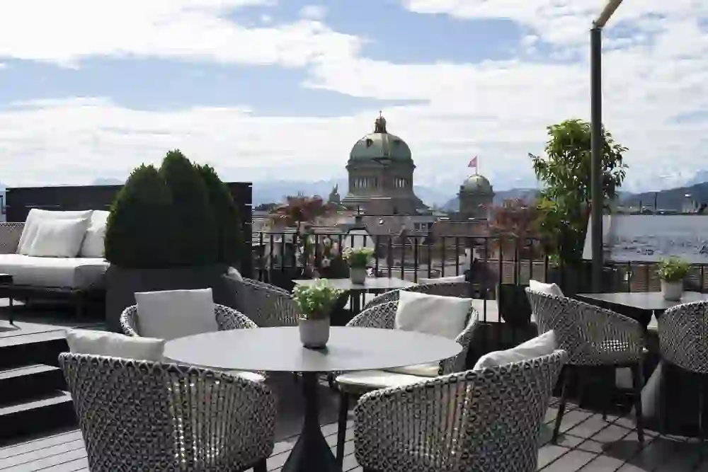 Une terrasse élégante sur le toit avec d'élégants sièges et une vue imprenable sur la vieille ville de Berne et les Alpes. L'atmosphère chaleureuse et la douce lumière du soleil invitent à des moments de détente.