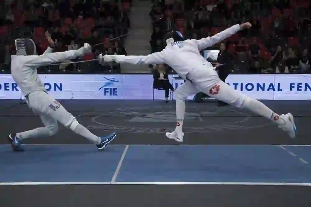 L'immagine mostra un momento emozionante della scherma a pinze. Lo schermidore sulla destra sferra un potente attacco mentre il suo avversario schiva. La tensione è palpabile, il pubblico segue l'avvincente competizione con concentrazione e fascino.