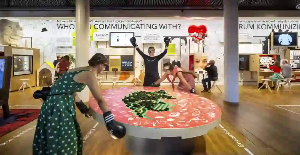 Die Ausstellung im Museum für Kommunikation pulsiert vor Leben; Besucher interagieren spielerisch und erkunden neugierig die vielfältigen Exponate.