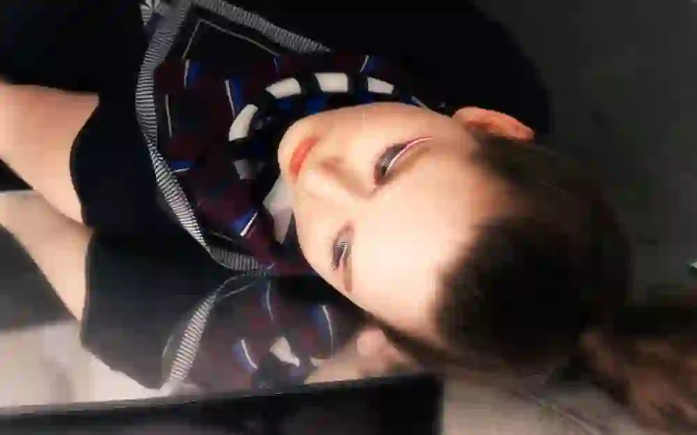 Das Foto zeigt eine Person mit geschlossenen Augen, entspannt und nachdenklich, mit dem Kopf auf einer reflektierenden Oberfläche liegend, was eine ruhige und introspektive Stimmung vermittelt.