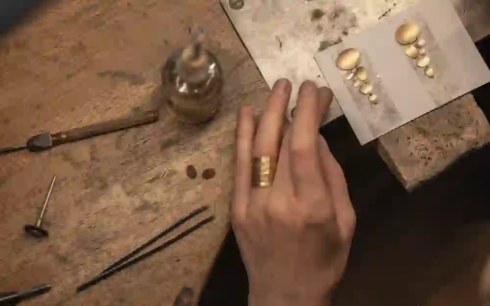 The picture shows hands carrying out a jewellery-making process with tools and materials on an old work table. It radiates concentration and craftsmanship and shows the beauty of the creative process.