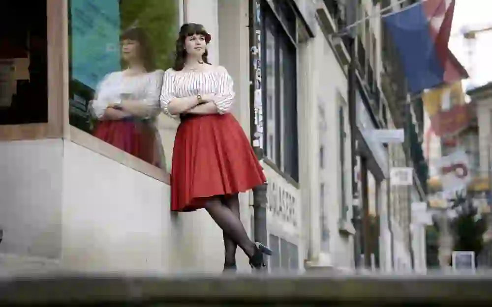 L'immagine mostra una persona sicura di sé, vestita di un vivace abbigliamento rosso e bianco, in posa in una strada di Berna. Il suo riflesso e la sua posizione determinata conferiscono alla foto un'aura potente e positiva.