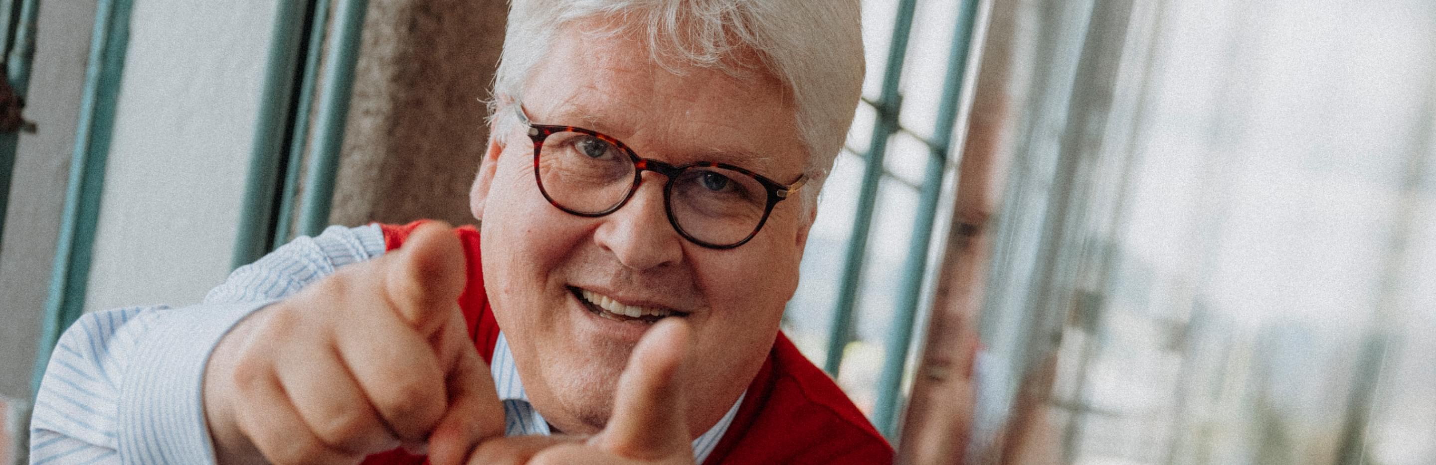 Sepp Hochreiter standing indoors by a window and pointing playfully toward the camera