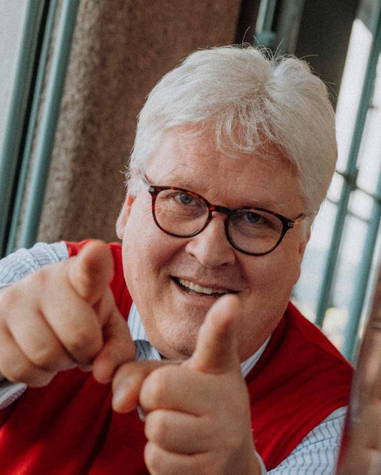 Sepp Hochreiter standing indoors by a window and pointing playfully toward the camera