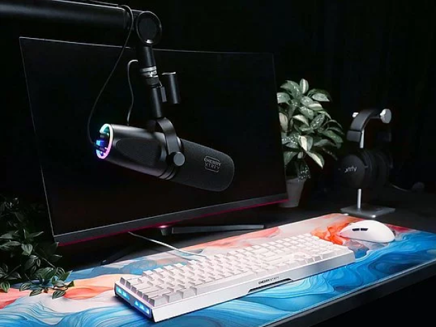 Ein eleganter Schreibtisch mit einer weißen Tastatur von Cherry, einem großen Monitor, einem schwarzen Mikrofon an einem Galgenarm, schwarzen Kopfhörern und einer Topfpflanze im Hintergrund.