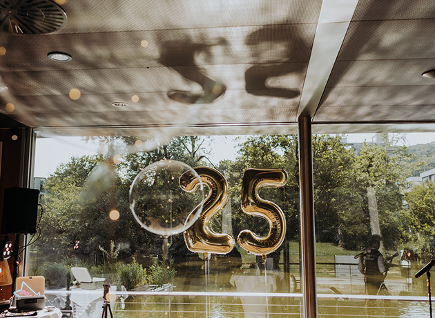 Goldene Ballons in Form der Zahl 25 werden im Innenbereich in der Nähe eines Fensters ausgestellt, im Hintergrund ist eine malerische Aussicht im Freien zu sehen.