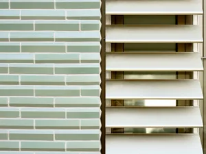 Detail of the jade-green three-dimensional ceramic tiles at the base of the Tübingen building beside golden louvres