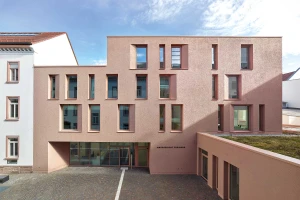 Modern building wing with a large glass façade featuring colorful graphic elements in the courtyard.