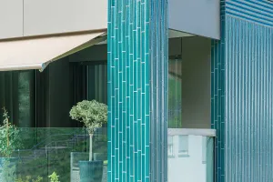 Mehrfamilienhaus in Willisau mit grüner Keramikfassade, vertikal strukturierten Elementen und großen Balkonen, umgeben von Grünflächen und Kieswegen.