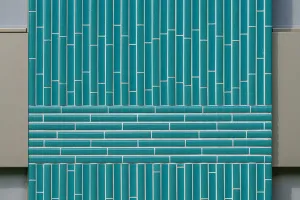 Mehrfamilienhaus in Willisau mit grüner Keramikfassade, vertikal strukturierten Elementen und großen Balkonen, umgeben von Grünflächen und Kieswegen.