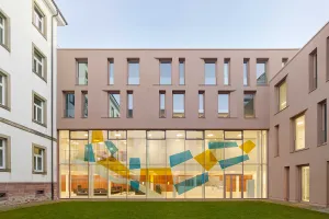 Modern building wing with a large glass façade featuring colorful graphic elements in the courtyard.