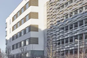 Tübingen office building with white render facade and blinds beside a curved, silvery metal facade.