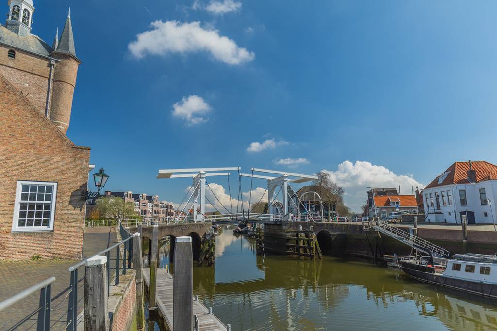 Ein Kanal mit einer Zugbrücke in einer europäischen Stadt mit historischen Backsteingebäuden und einem klaren blauen Himmel.