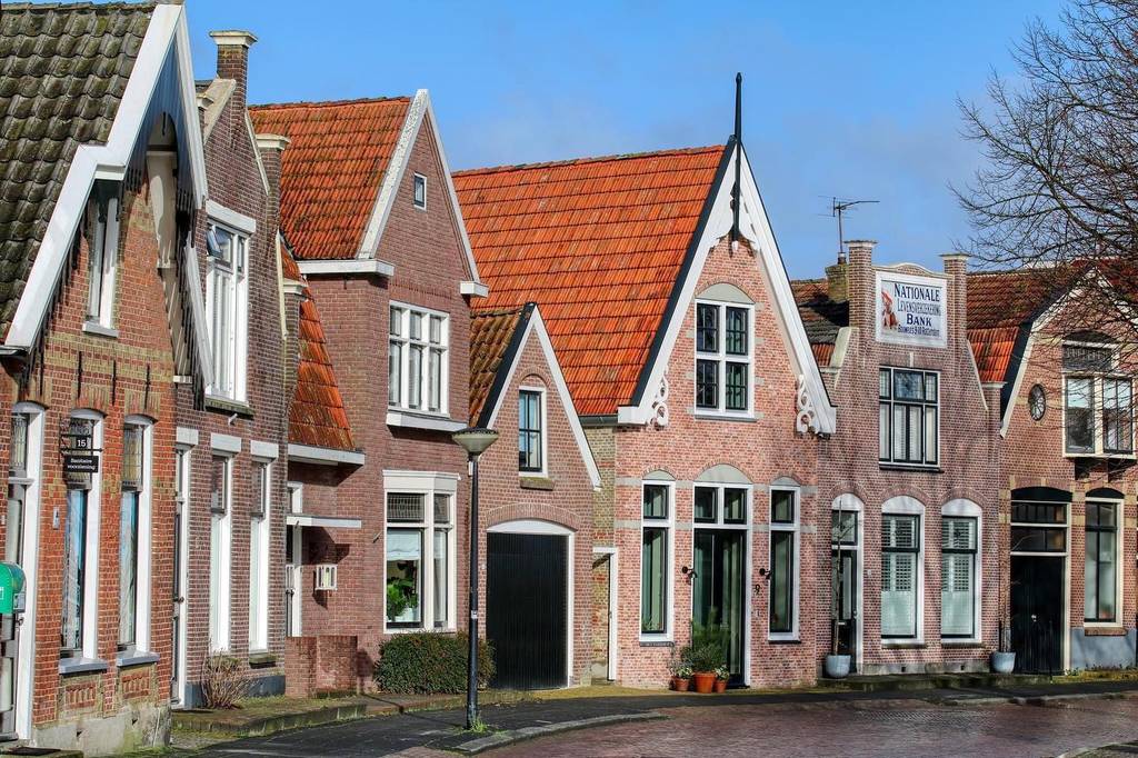 Eine Reihe charmanter, traditioneller Backsteinhäuser mit steilen Giebeldächern und weißen Zierleisten unter einem klaren blauen Himmel.