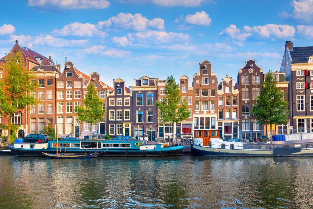 Gracht in Amsterdam mit traditionellen schmalen Häusern, Bäumen und Booten