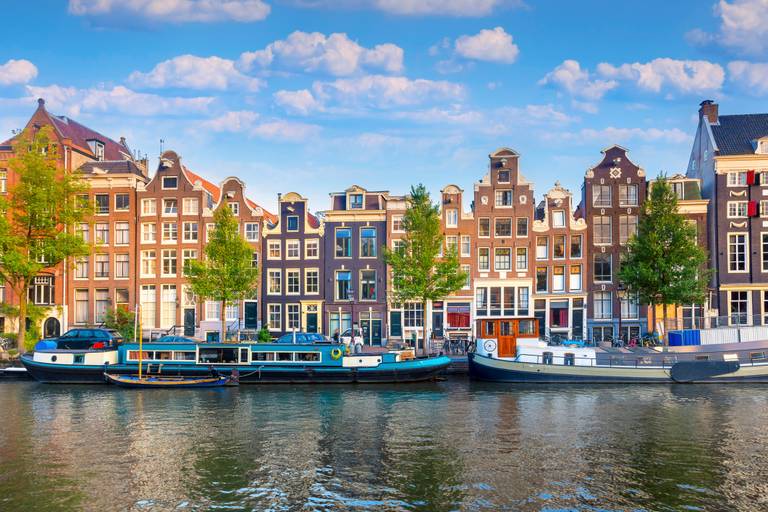 Gracht in Amsterdam mit traditionellen schmalen Häusern, Bäumen und Booten
