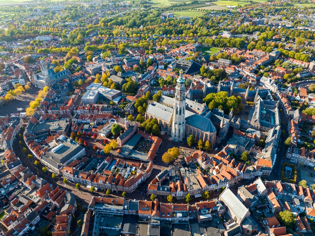 Luftaufnahme einer historischen europäischen Stadt mit einer großen Kathedrale, umgeben von Gebäuden mit roten Dächern und üppigen grünen Bäumen.