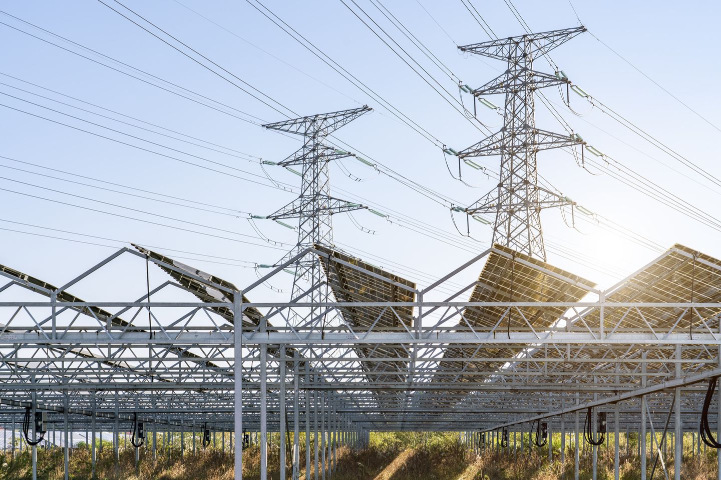 Eine Solaranlage steht vor zwei Strommasten auf einem Feld. © lingqi xie / Moment via Getty Images