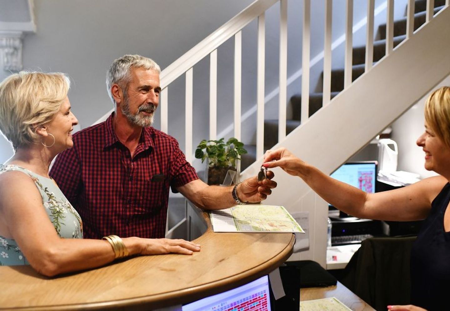 Sanfter Tourismus: Älteres Paar nimmt einen Zimmerschlüssel an der Rezeption von einer Frau entgegen. © wilpunt / E+ via Getty Images
