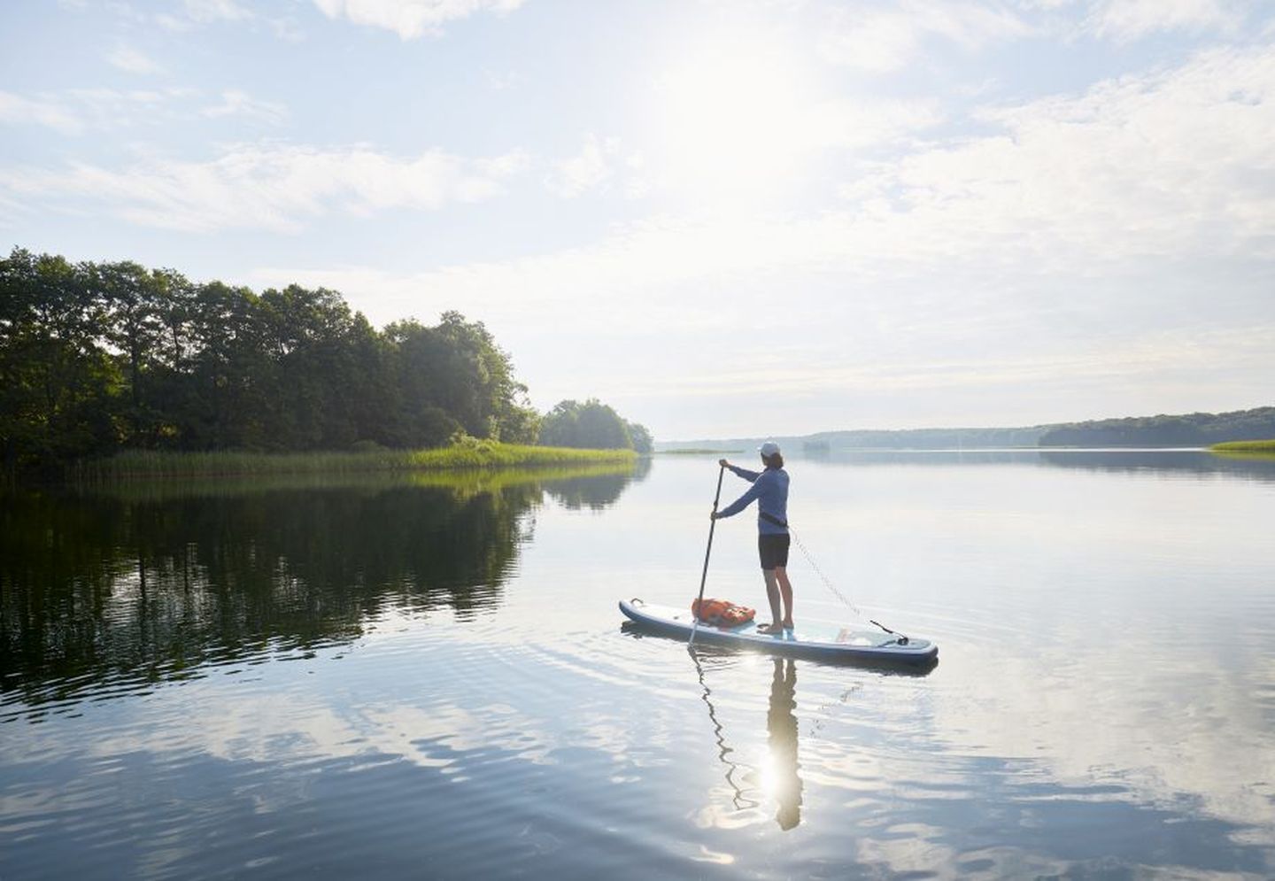 Eine Frau beim SUP auf einem idyllischen See im Sommer.