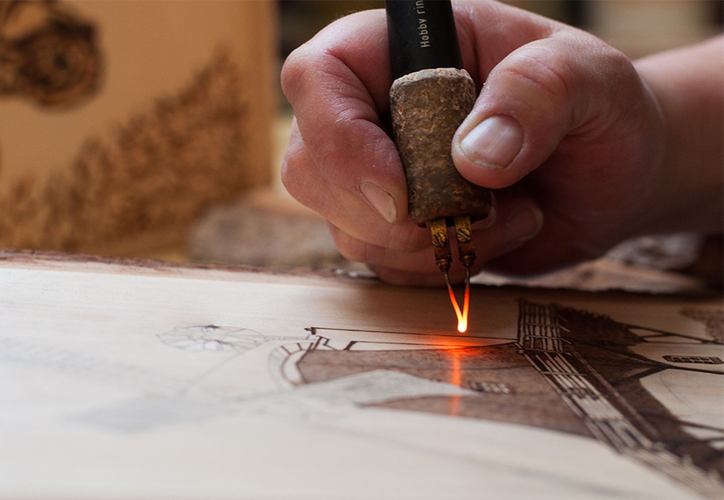 Brandmalerei: Eine Hand führt eine rot glühende Brennspitze über das Holz.