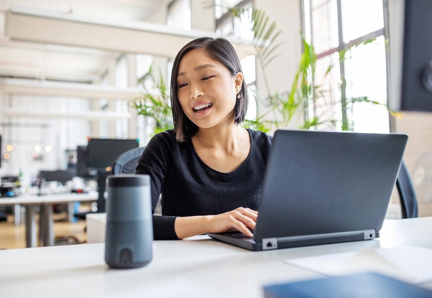 Eine Frau sitzt im Büro und spricht mit ihrem Sprachassistenten-Lautsprecher. © alvarez / E+