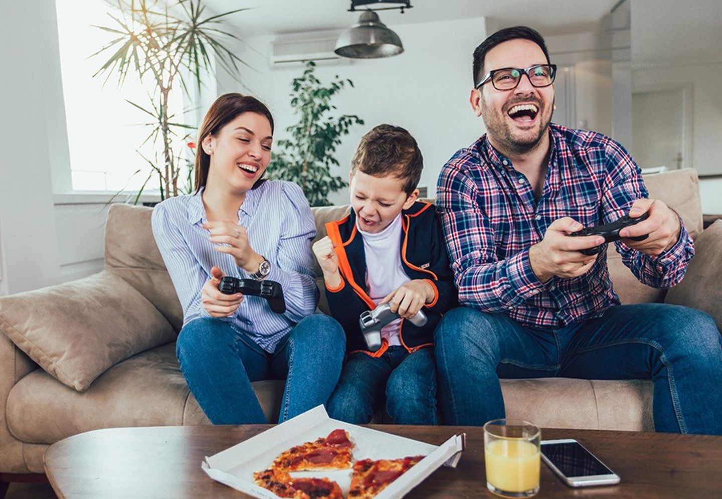 Eltern und Kind sitzen mit Controllern auf der Couch