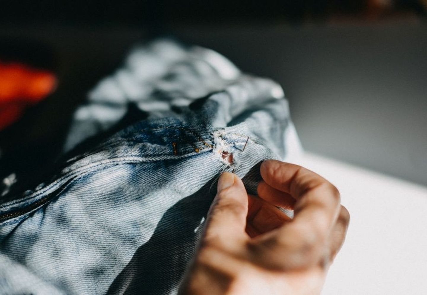 Eine Hand flickt ein Kleidungsstück aus Jeansstoff.