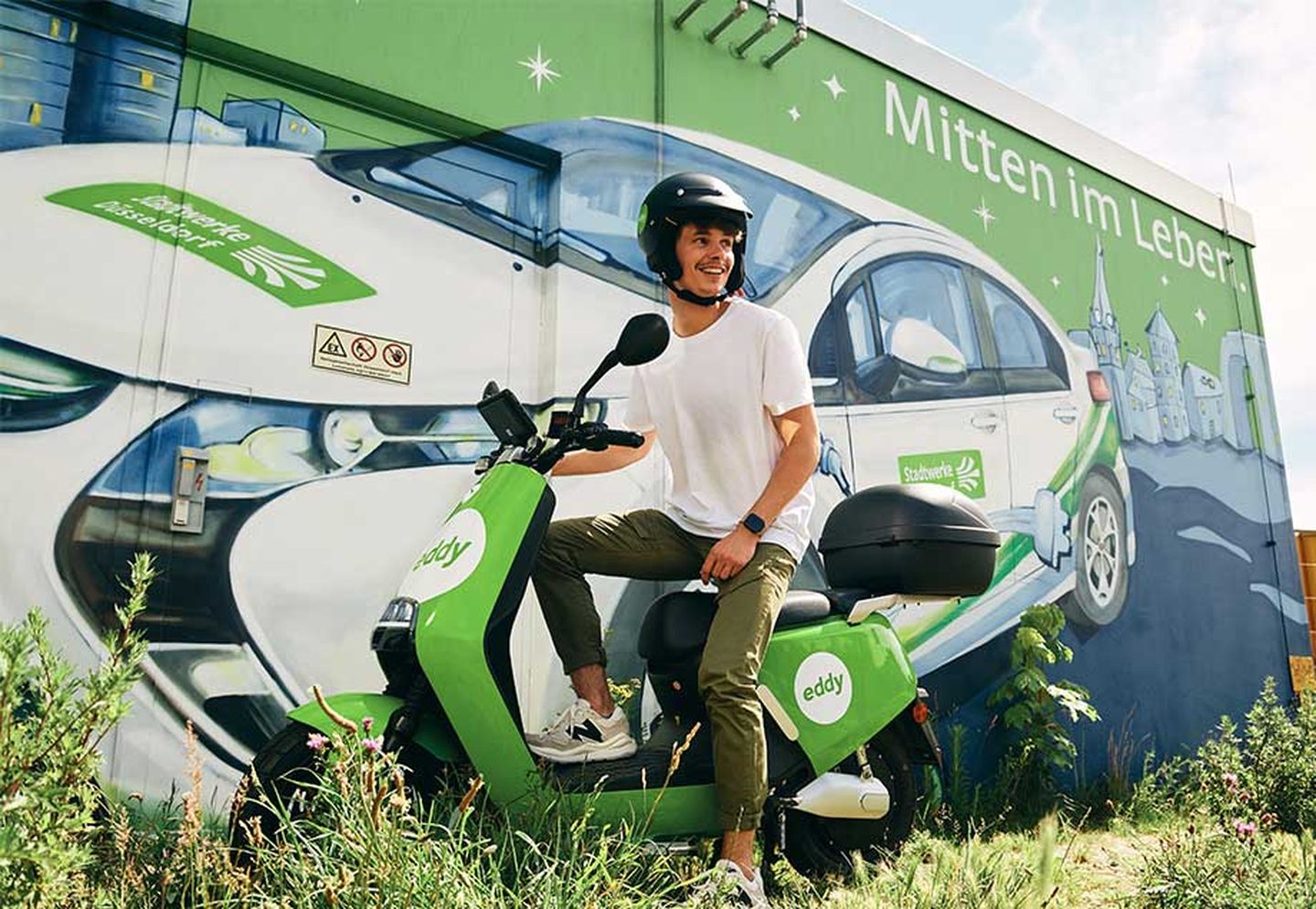 Ein E-Roller mit Mann vor einem Traffohäuschen der Stadtwerke Düsseldorf