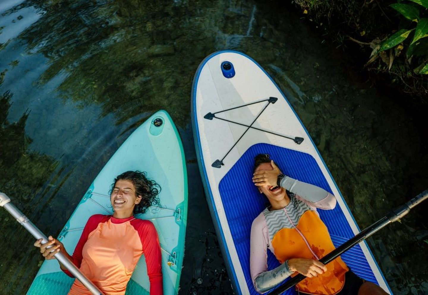 Zwei lachende Frauen, die auf ihren SUP-Boards liegen. © AleksandarNakic / E+ via Getty Images