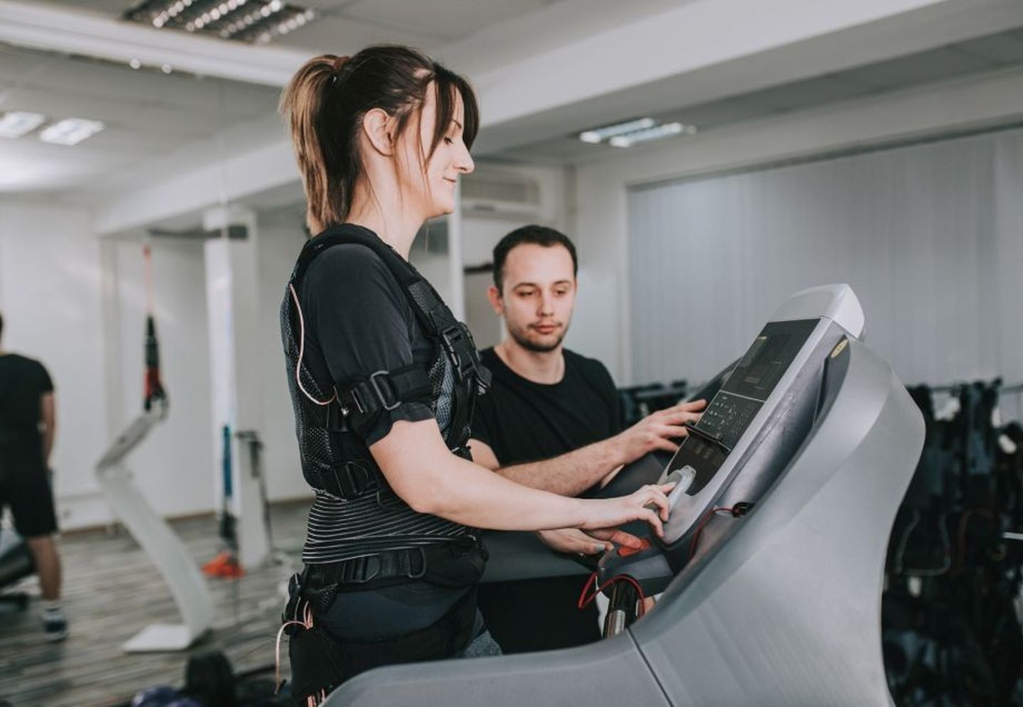 EMS-Training: Ein Trainer leitet seine Kundin auf dem Laufband an, während sie mit einem Funktionsanzug samt Elektroden trainiert.