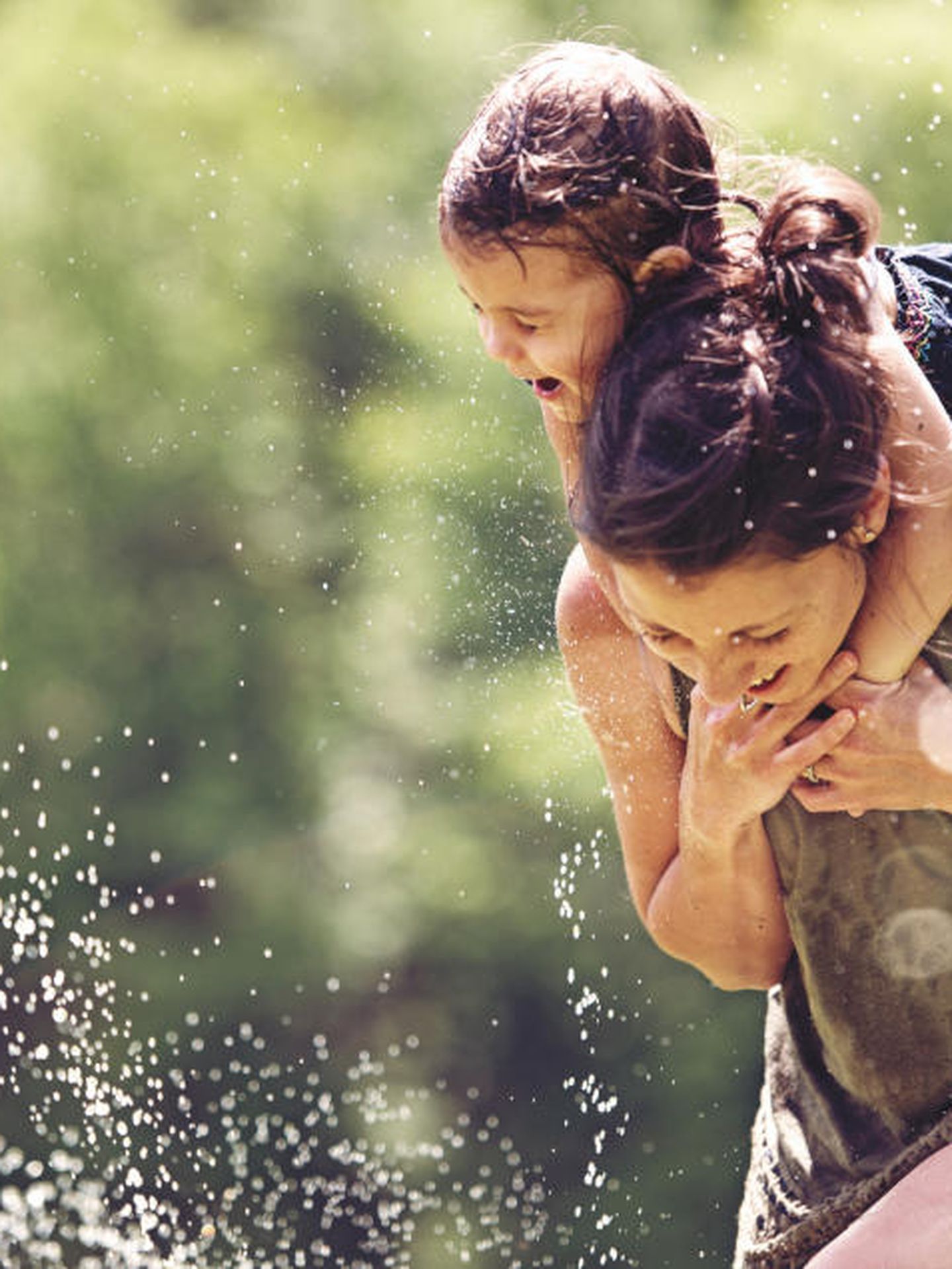 Nahaufnahme von Mutter und Kind, die auf einem Wasserspielplatz durch eine Wasserfontäne laufen. © lisegagne / E+ via Getty Images