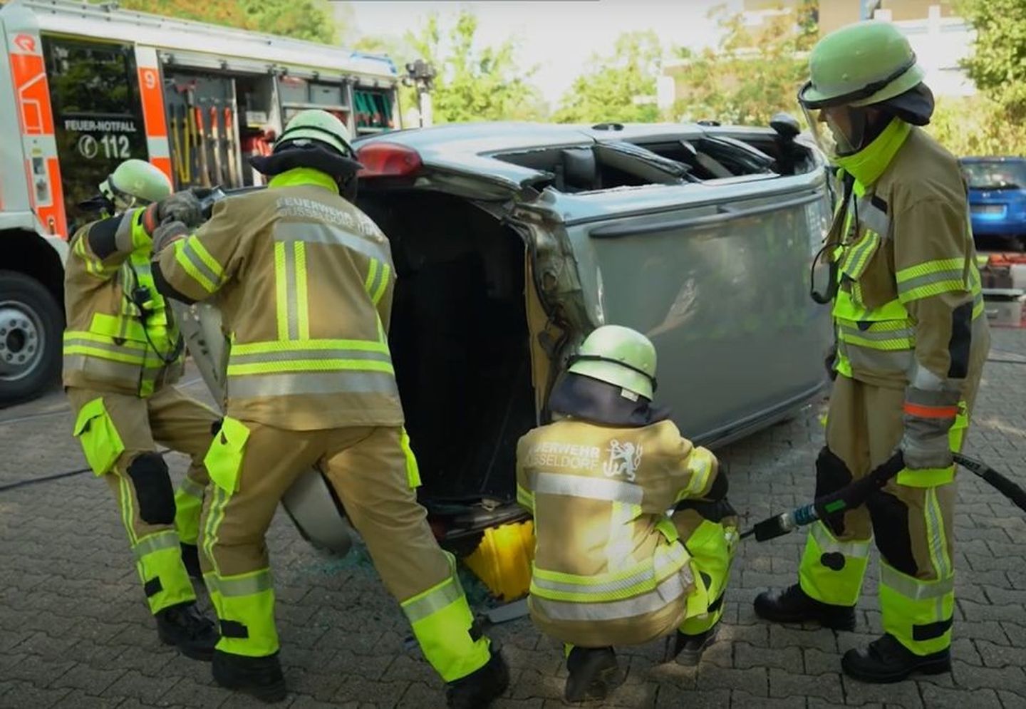 Schüler:innen der Feuerwehrschule Düsseldorf schneiden auf einem Übungsplatz der Feuerwehr ein verunfalltes Fahrzeug von der Dachseite auf. 