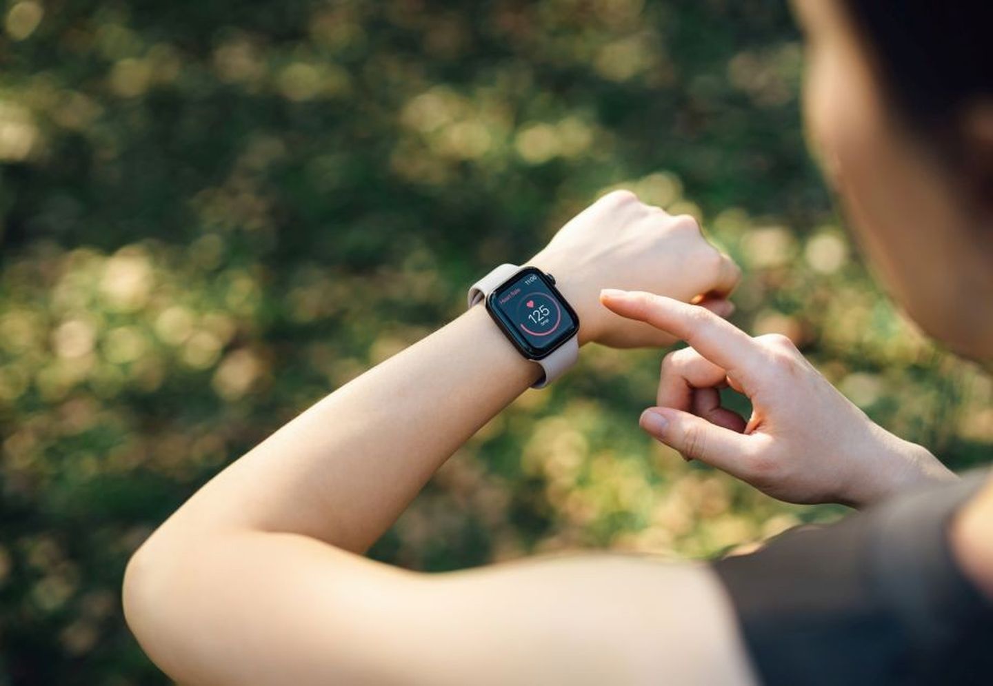 Eine Frau schaut auf ihre Smartwatch, die die Herzfrequenz beim Training im Park anzeigt. 