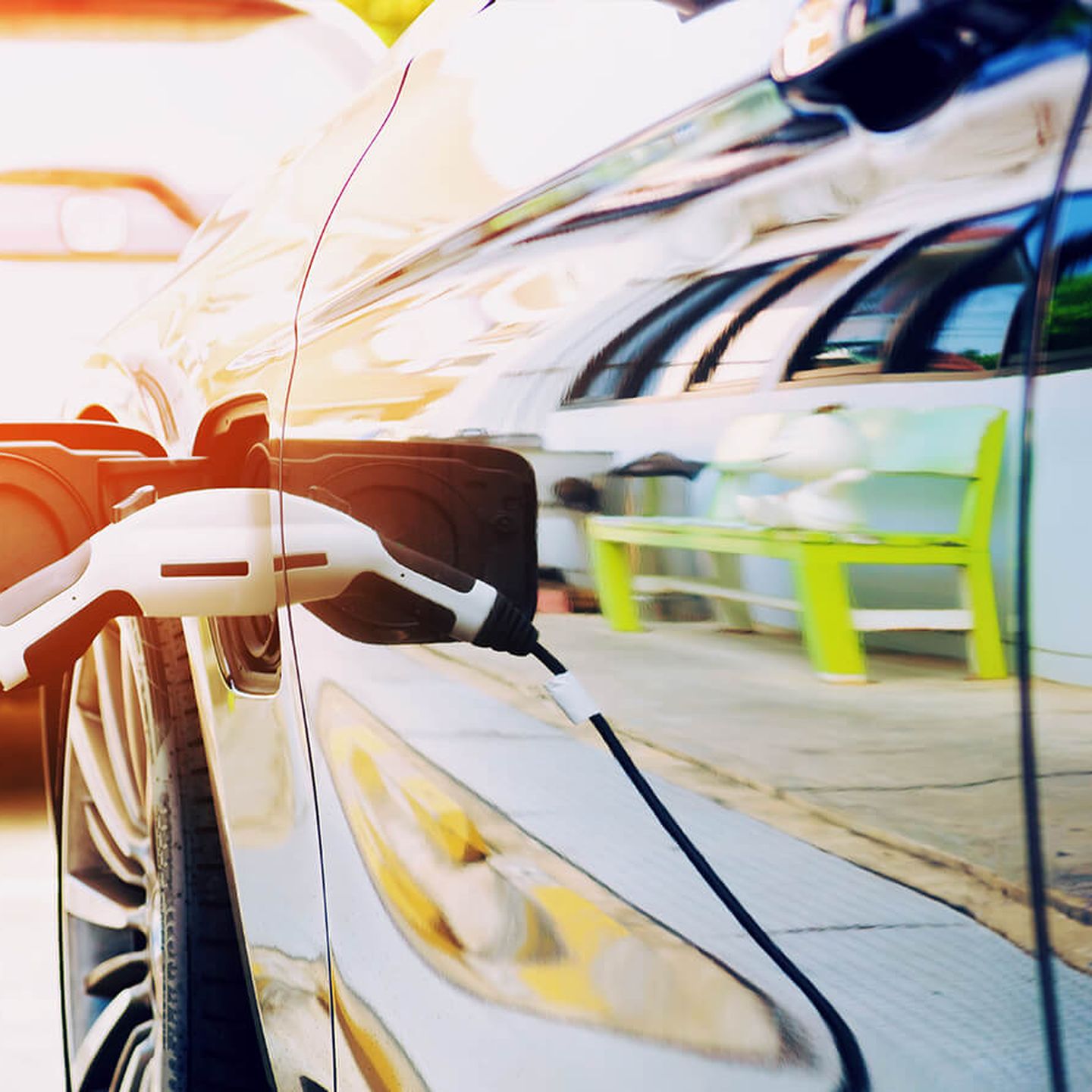 Ladestecker in E-Auto-Steckdose gesteckt. Im Lack der Autotür spiegelt sich eine giftgrüne Sitzbank.