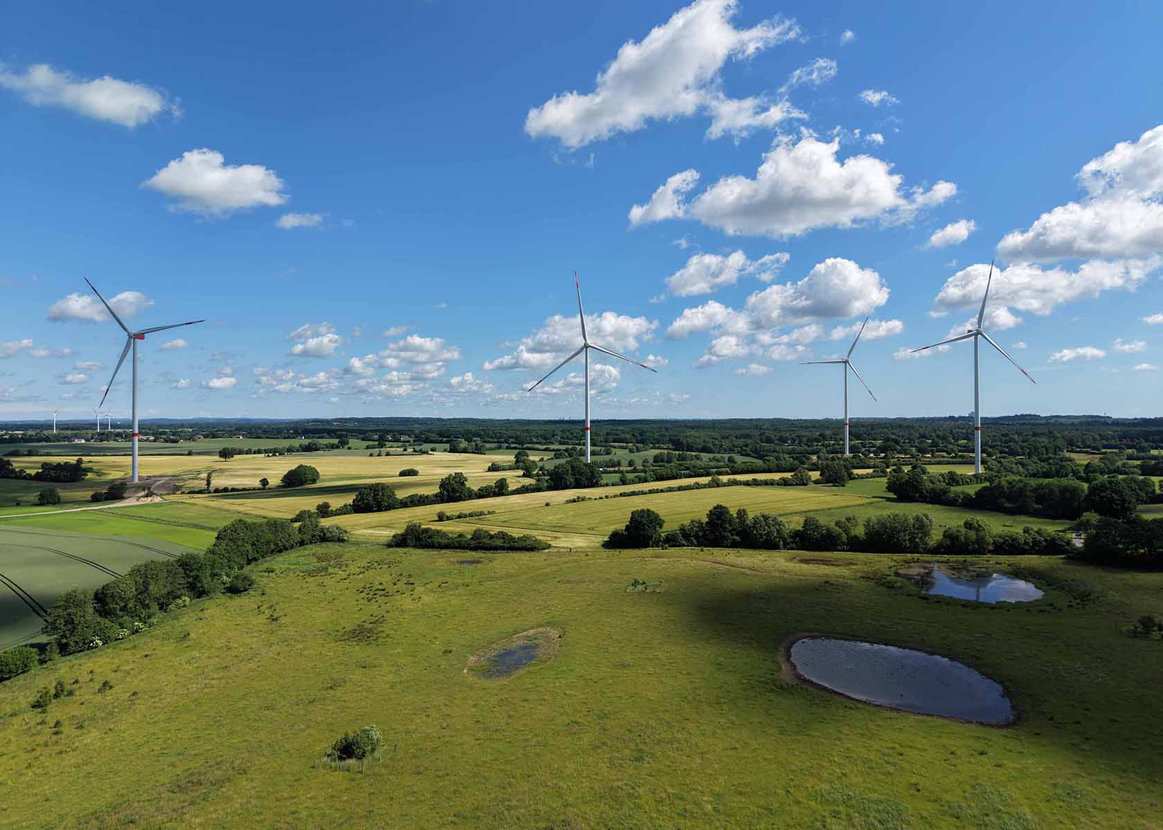 Windkraftanlagen auf einer grünen Wiese unter blauem Himmel mit vereinzelten Wolken