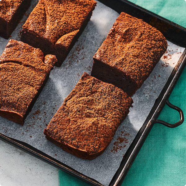 Sliced chocolate brownies dusted with cocoa powder arranged on a lined baking tray shot from above