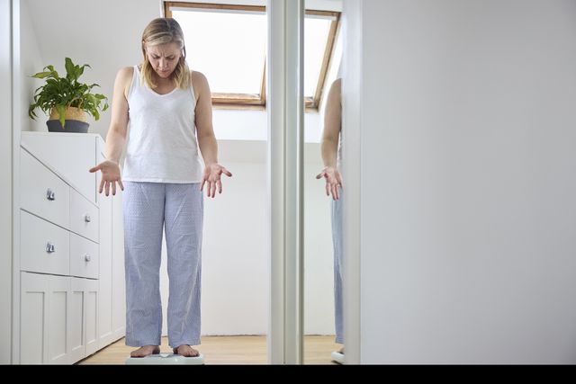 menopausal woman looking accusingly at the scales she stands on
