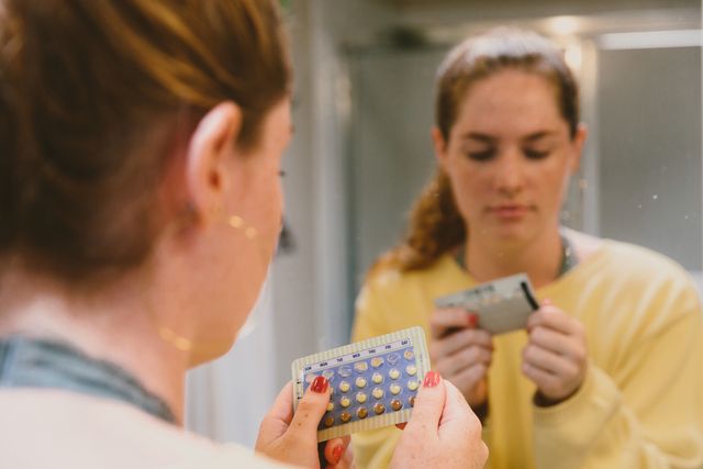 woman in mirror inspecting birth control medication
