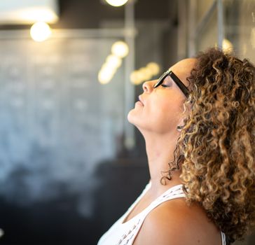 Woman with curly hair and glasses leaning her head against a glass window