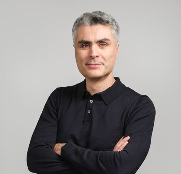 Man smiling with arms crossed in black polo shirt