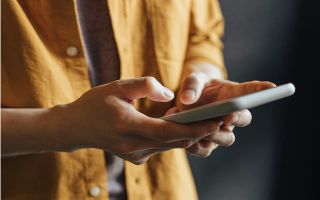 A close-up of a person in a yellow shirt holding and using a smartphone