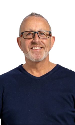 An older man with short grey hair and glasses wearing a navy v-neck top smiling warmly against a mint green background