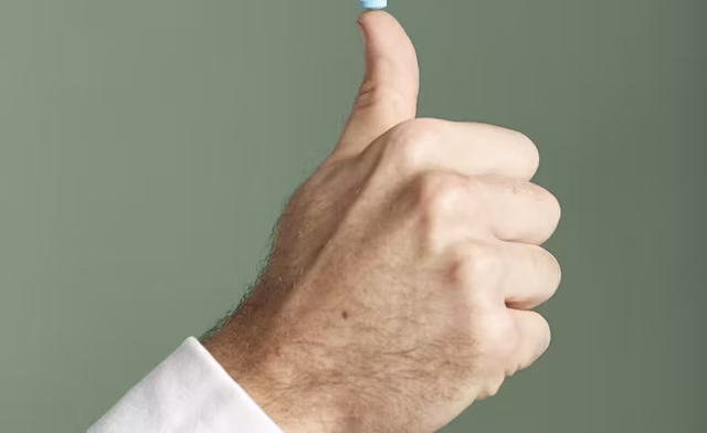 man's hand balancing little blue pill on thumb