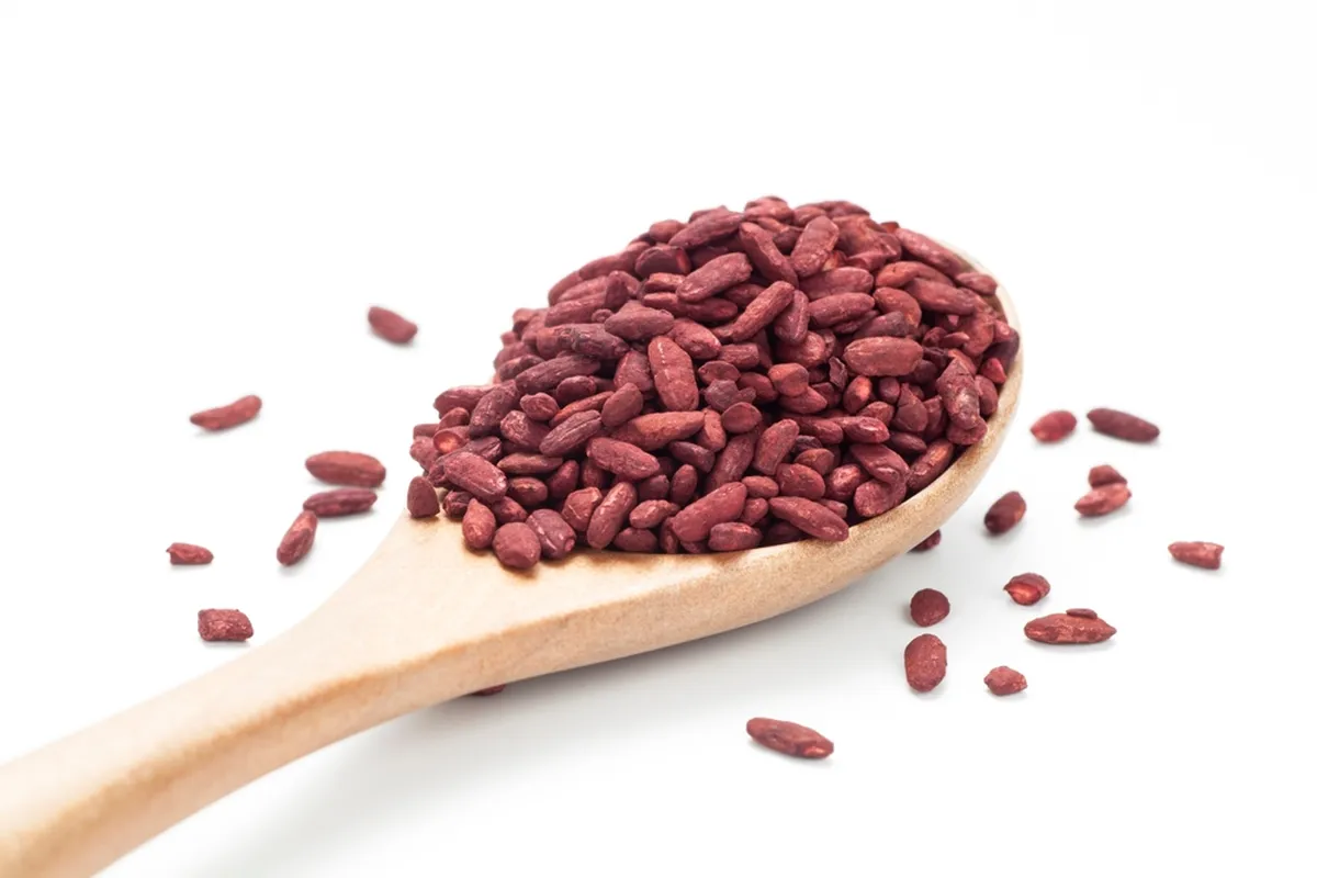 A wooden spoon holding red yeast rice on a white background, with a few grains scattered around.