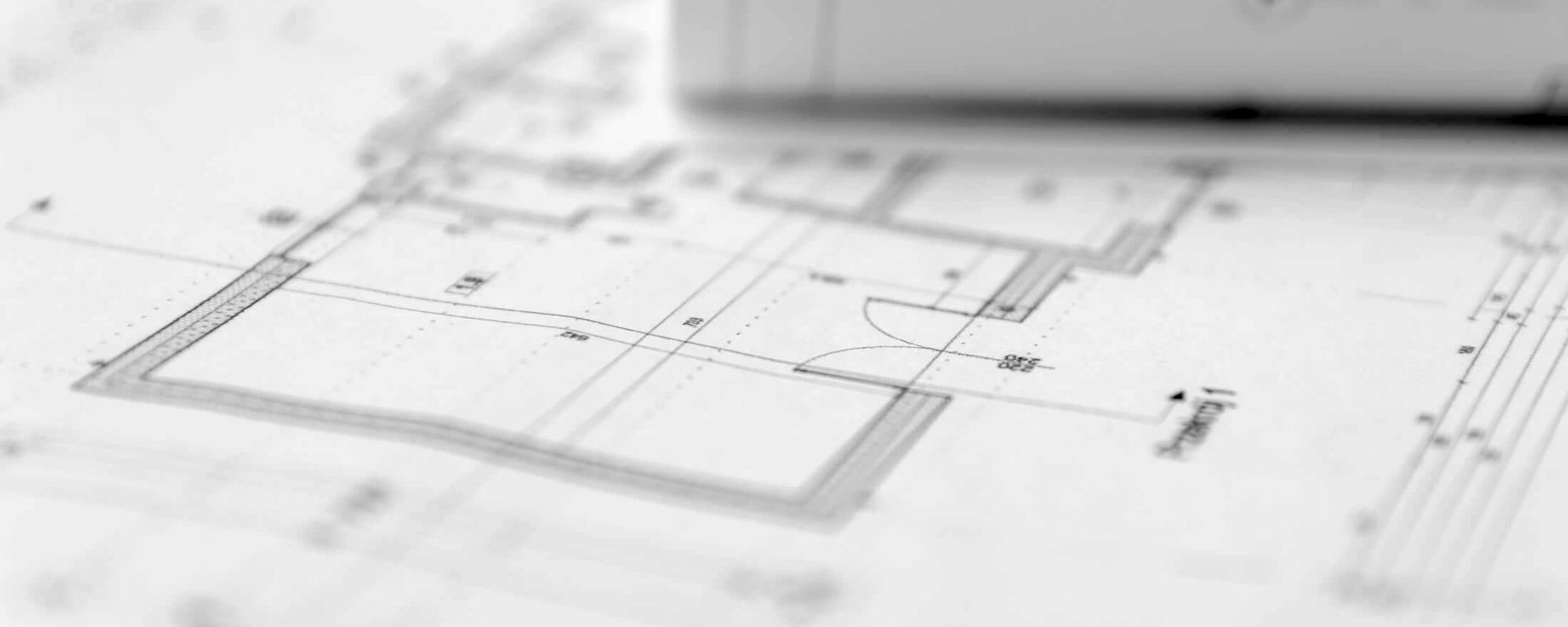 Close-up of architectural blueprints with detailed floor plans and measurements, featuring a partially rolled-up section on the right.