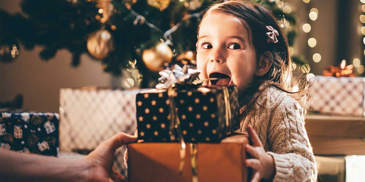 Ein Mädchen sitzt aufgeregt vor ihren Weihnachtsgeschenken