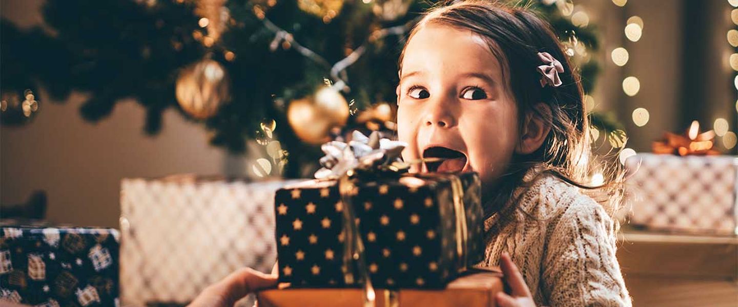 Ein Mädchen sitzt aufgeregt vor ihren Weihnachtsgeschenken