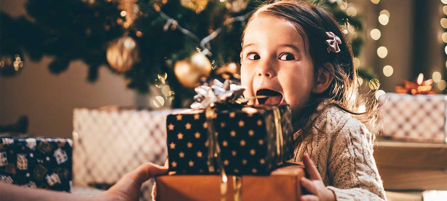 Ein Mädchen sitzt aufgeregt vor ihren Weihnachtsgeschenken