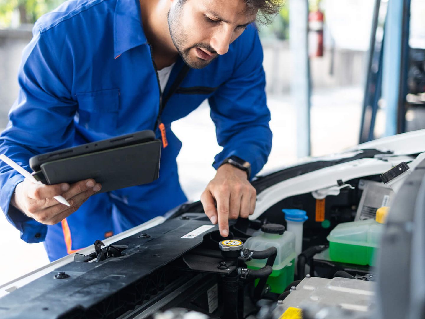 Ein Mechaniker kontrolliert Komponenten eines E-Autos an der geöffneten Motorhaube.